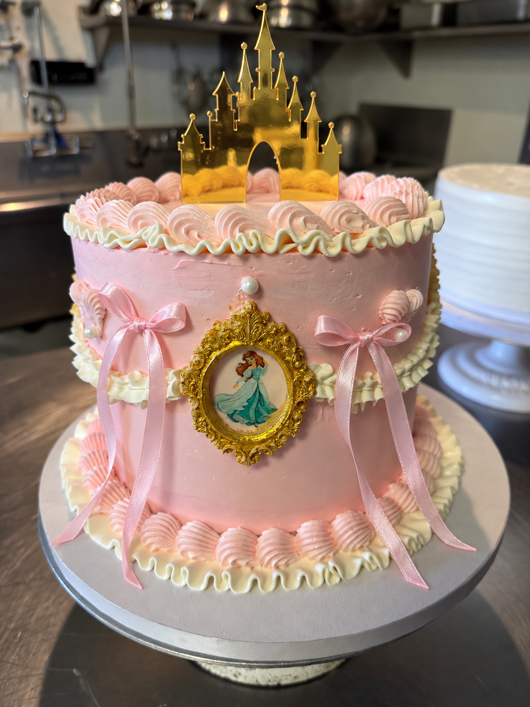 Pink Ariel birthday cake with ivory buttercream, pink ribbon bows, and a gold castle topper