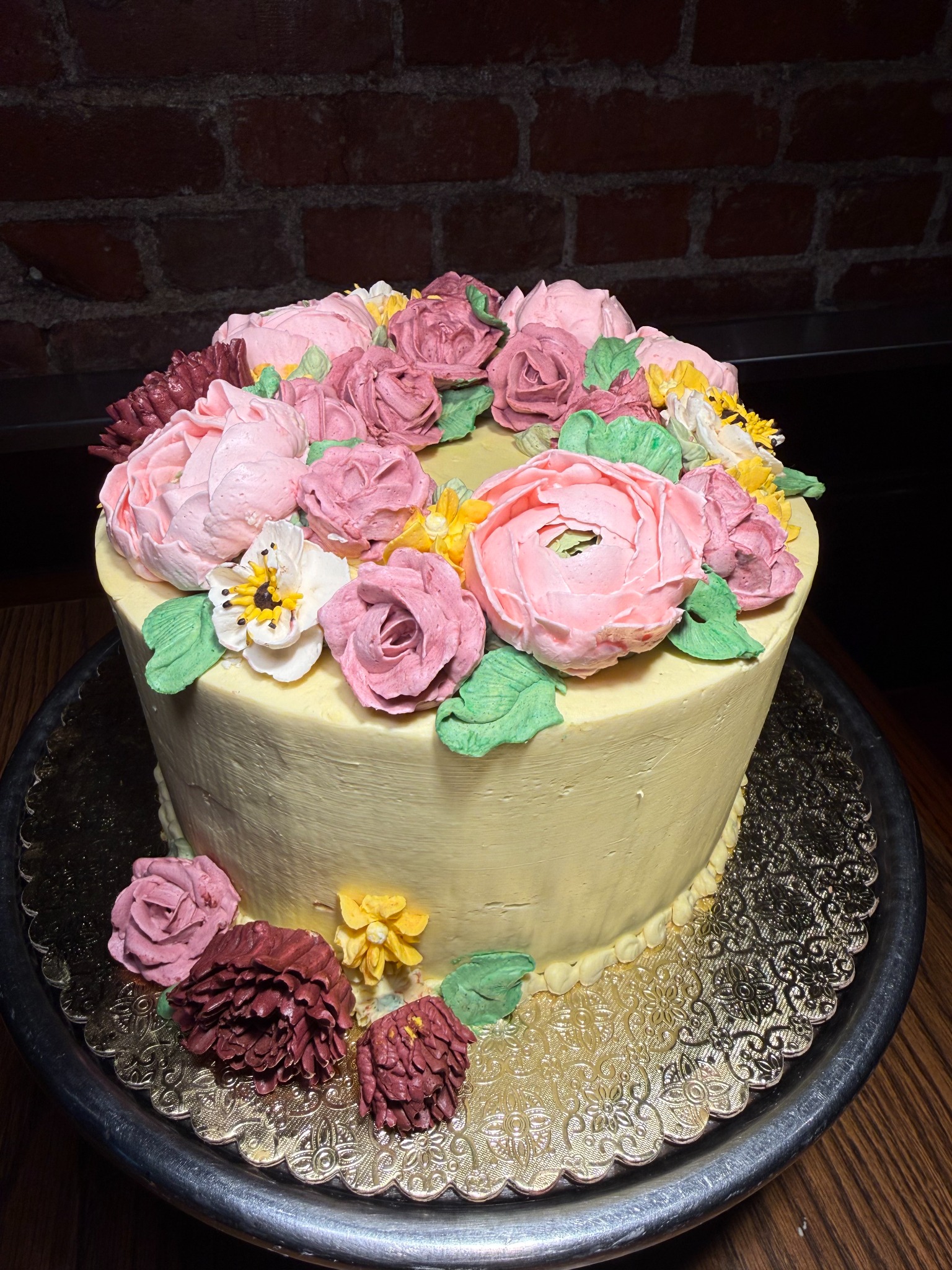 Pale yellow cake topped with large pink and mauve buttercream flowers