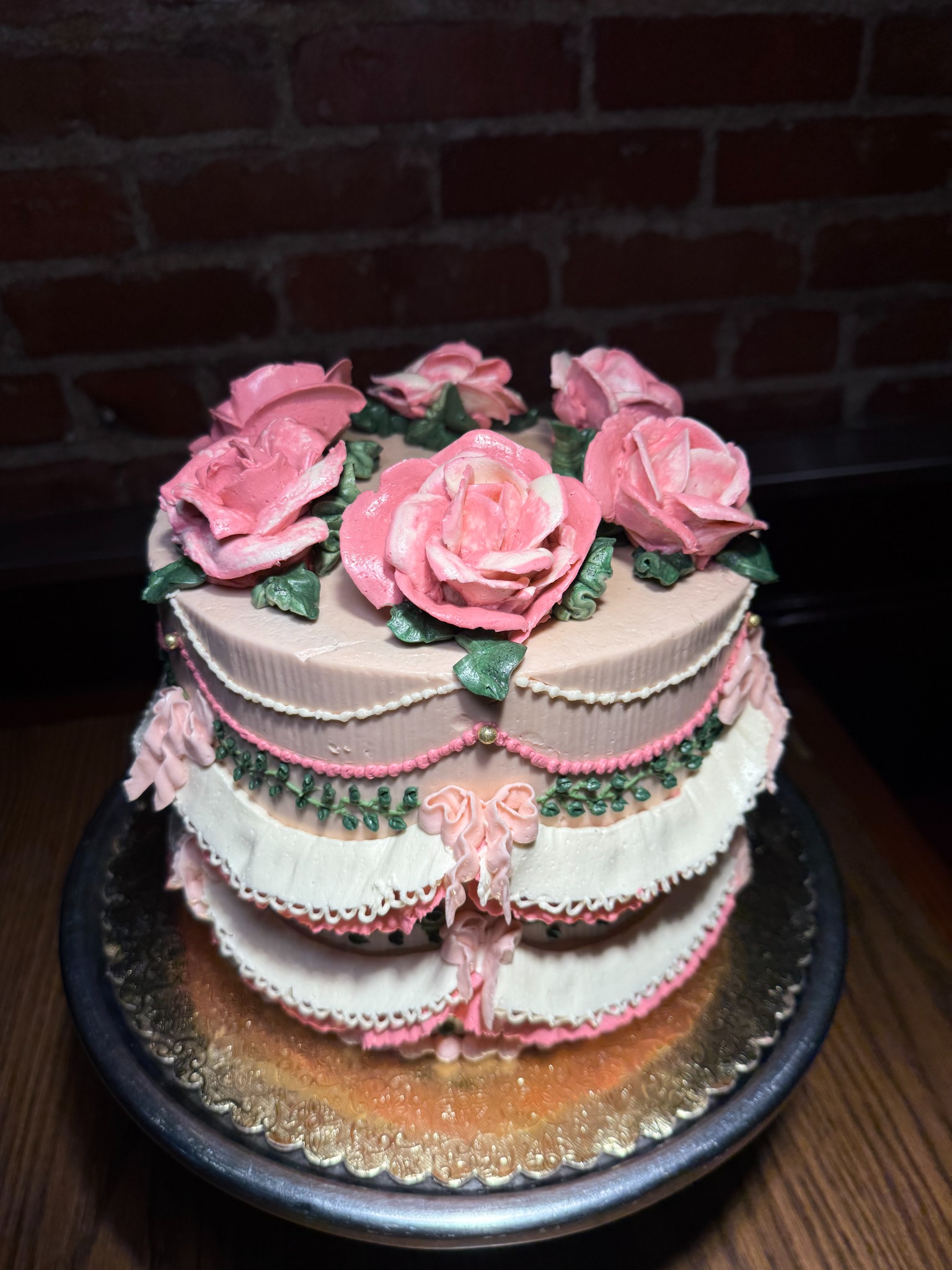 Two-tier pink and ivory cake with piped roses, green garlands, and pink bows